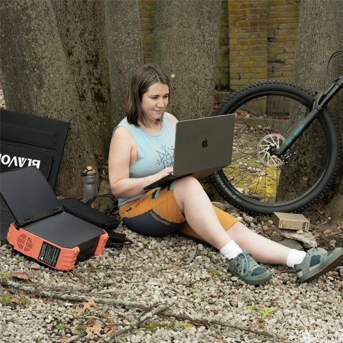 Angela Johnson, founder of The Real Cat Labs, working on a laptop outdoors next to a mountain bike with portable computing equipment and a solar panel.