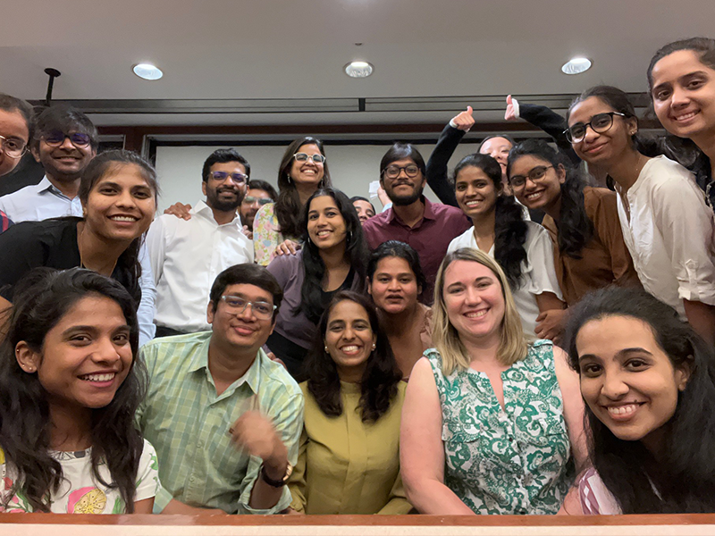 Angela Johnson with a diverse group of smiling graduate students in a university classroom after a hands-on regulatory strategy session.