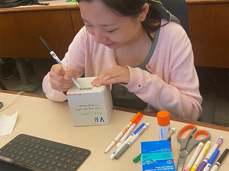 A Northeastern University graduate student using Crayola markers to mock up regulatory labeling for a medical device, demonstrating the hands-on teaching approach that bridges design thinking with FDA compliance strategy.